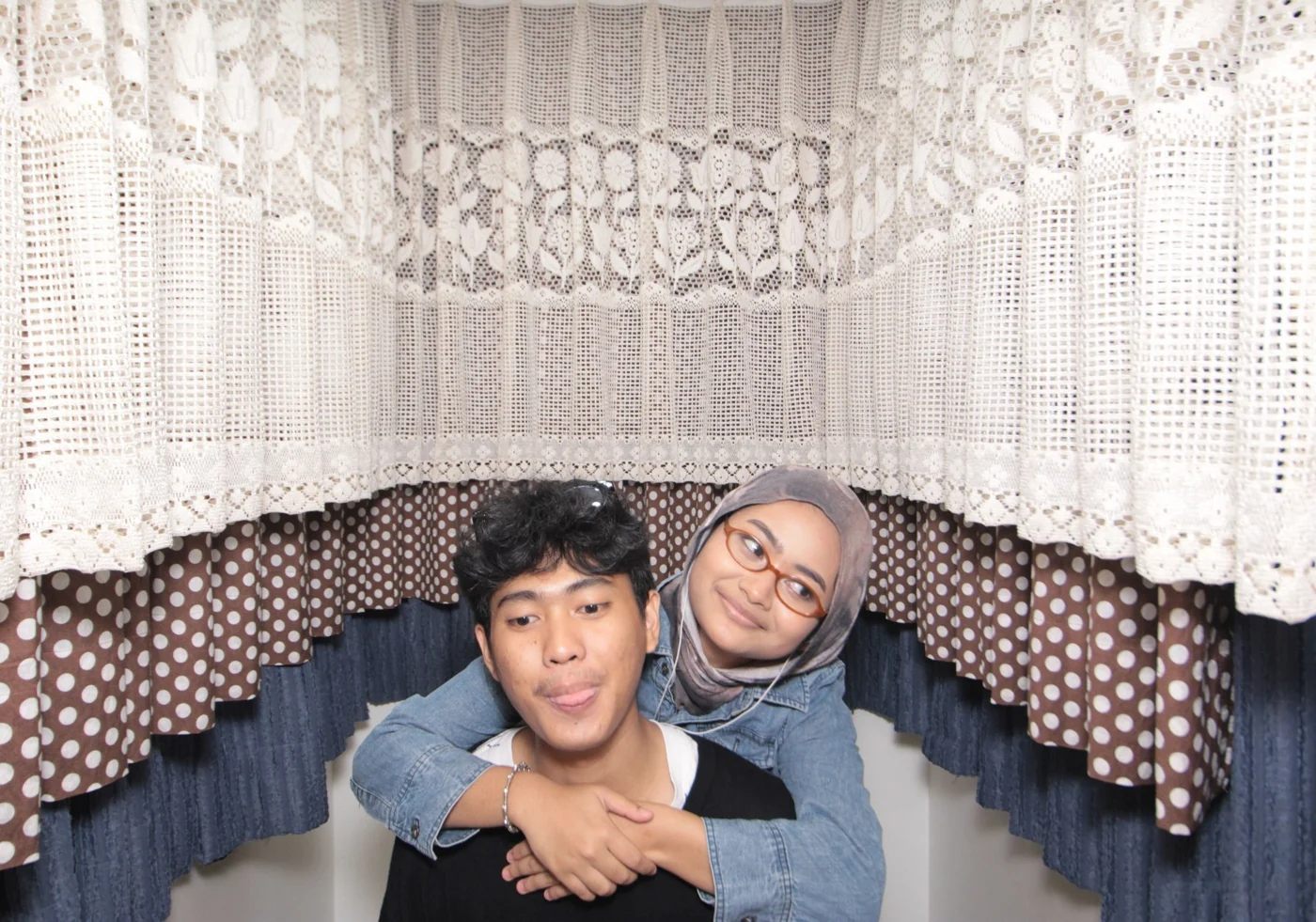 A playful photo booth pose with her arms around his shoulders